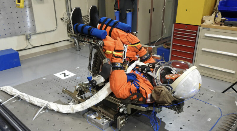 NASA's "Moonikin" paspop, gekleed in een oranje ruimtepak, zittende in lanceerpositie.