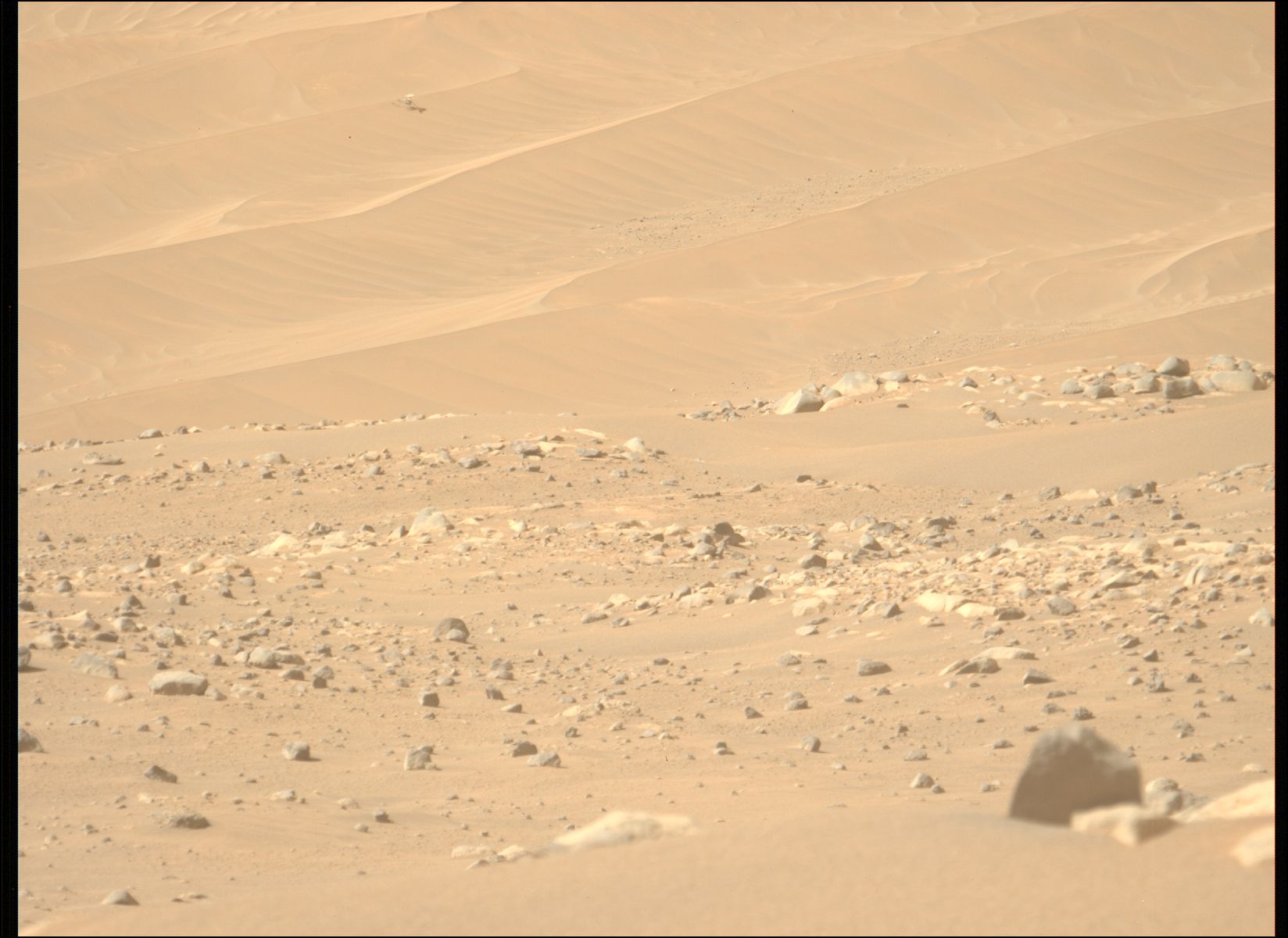 een kleine helikopter is roerloos te zien op een zandduin in de verte terwijl rode aarde en rotsen het tafereel vullen. 